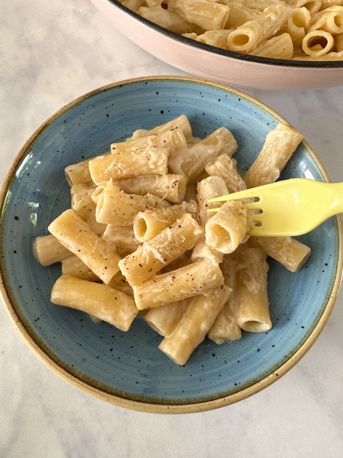 A blue bowl with a serving of broccoli stalk pasta in it and a kids plastic yellow spoon.