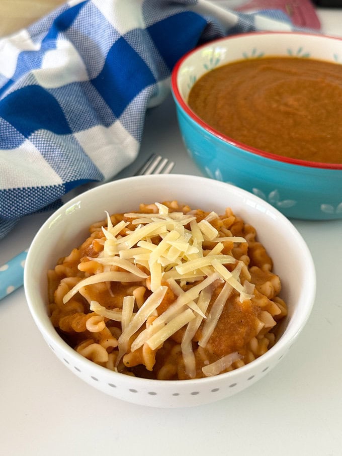 A white bowl with a serving of No Tomato Pasta with a sprinkling of grated cheddar cheese on top