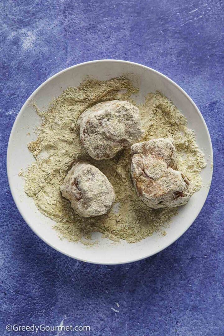 three pieces of oxtail dusted in a spiced flour in a white bowl on a blue tabletop