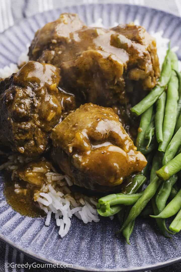 three pieces of oxtail served on white rice with green beans on a grey plate.