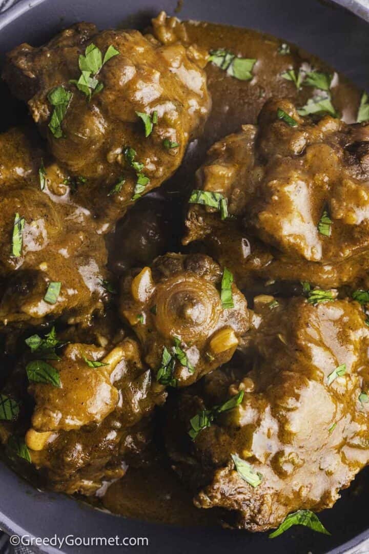 slow cooker oxtail served in a grey bowl, topped with chopped parsley.