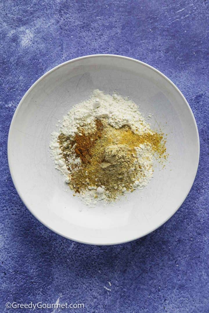 a white bowl with flour and ground spices on a blue background