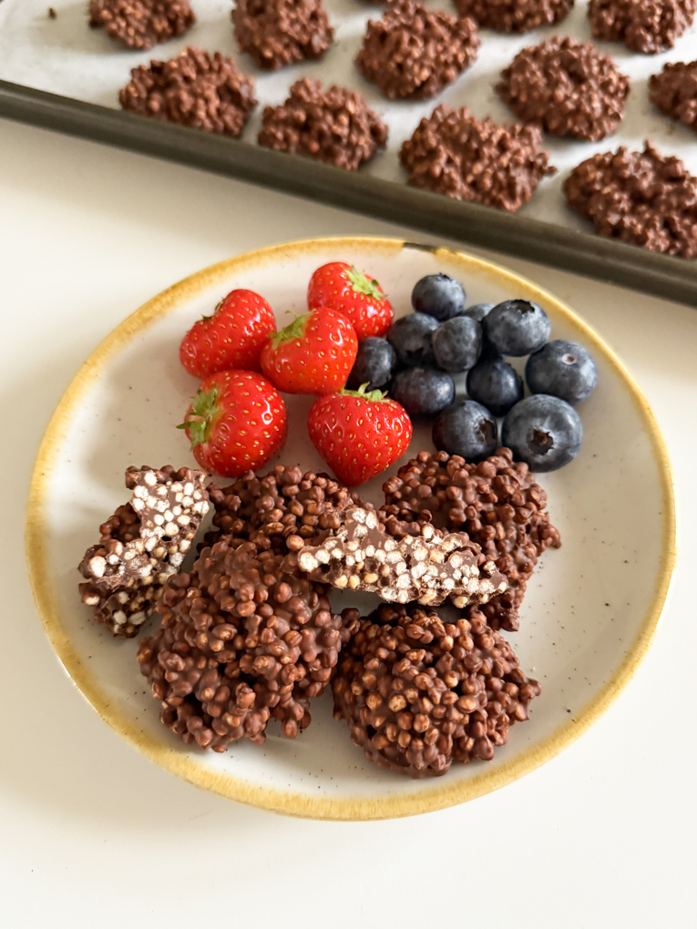 Five Chocolate Quinoa bites served on a round side plate with strawberries and blueberries.