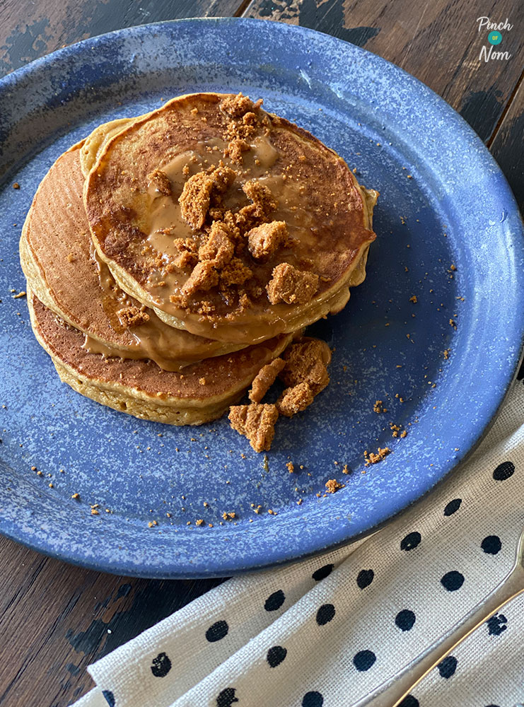 A table is set with a plate of Pinch of Nom's slimming-friendly Lotus Biscoff American Pancakes topped with a melty Biscoff drizzle and crushed Biscoff biscuits.