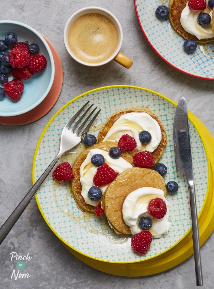 A table is set with Pinch of Nom's slimming-friendly Oat Pancakes, topped with fat-free yoghurt, honey, blueberries and raspberries.