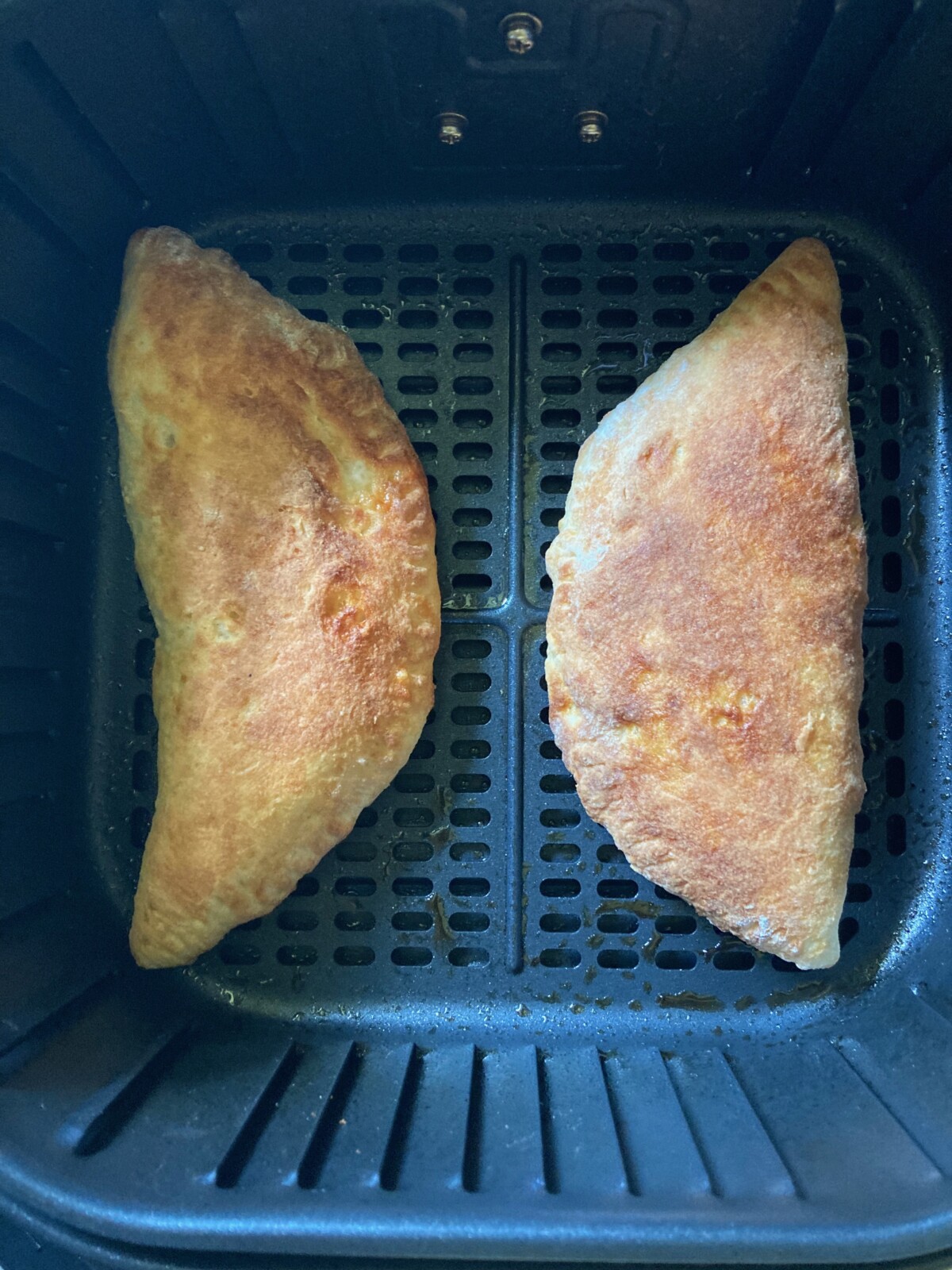 Two bean and cheese empanadas in air fryer basket.