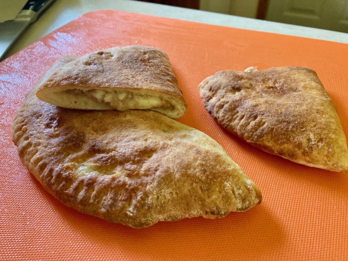 Fresh baked bean and cheese empanadas on orange cutting board.
