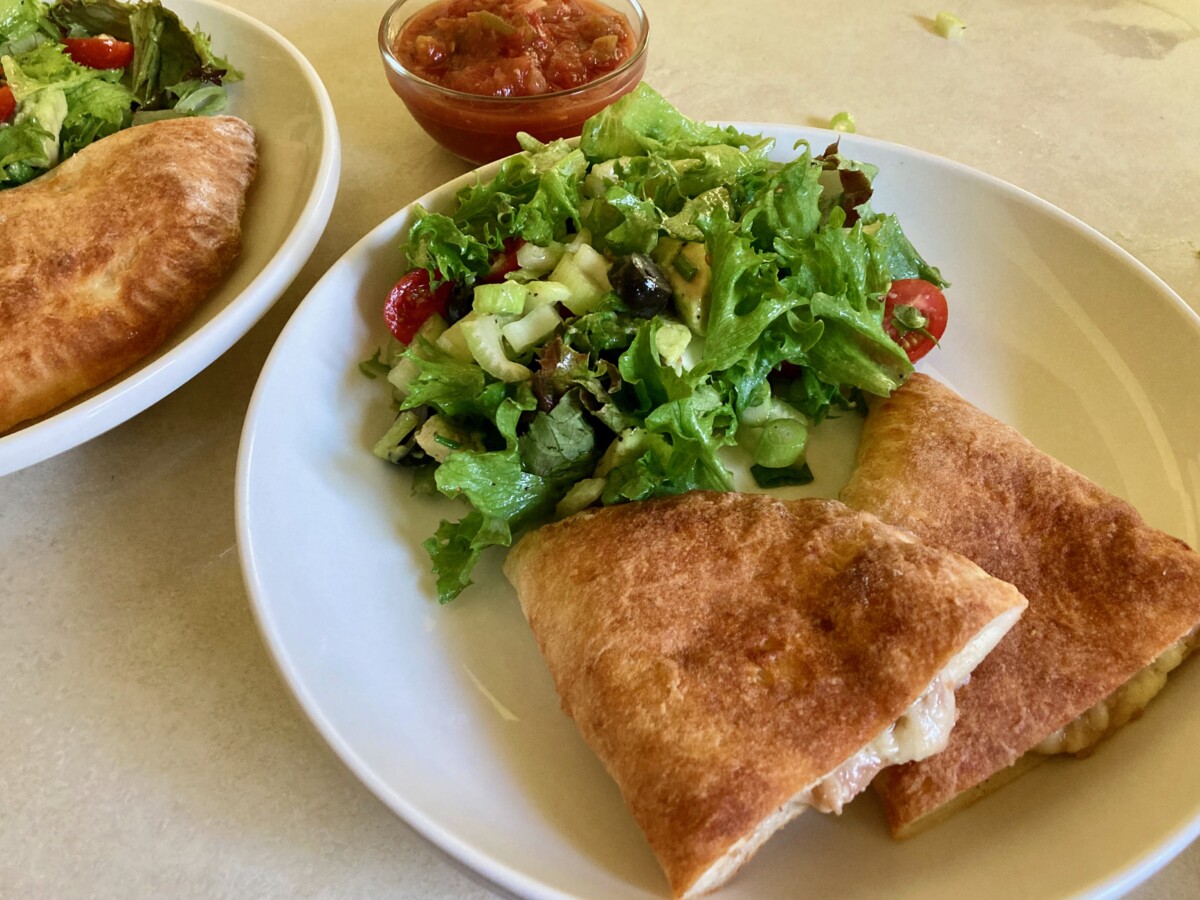 AIr Fryer Bean and Cheese Empanadas cut in half on white plate with salad and small bowl of salsa.